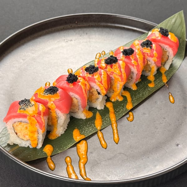 A sushi roll with tuna, orange sauce, and black caviar on a banana leaf.