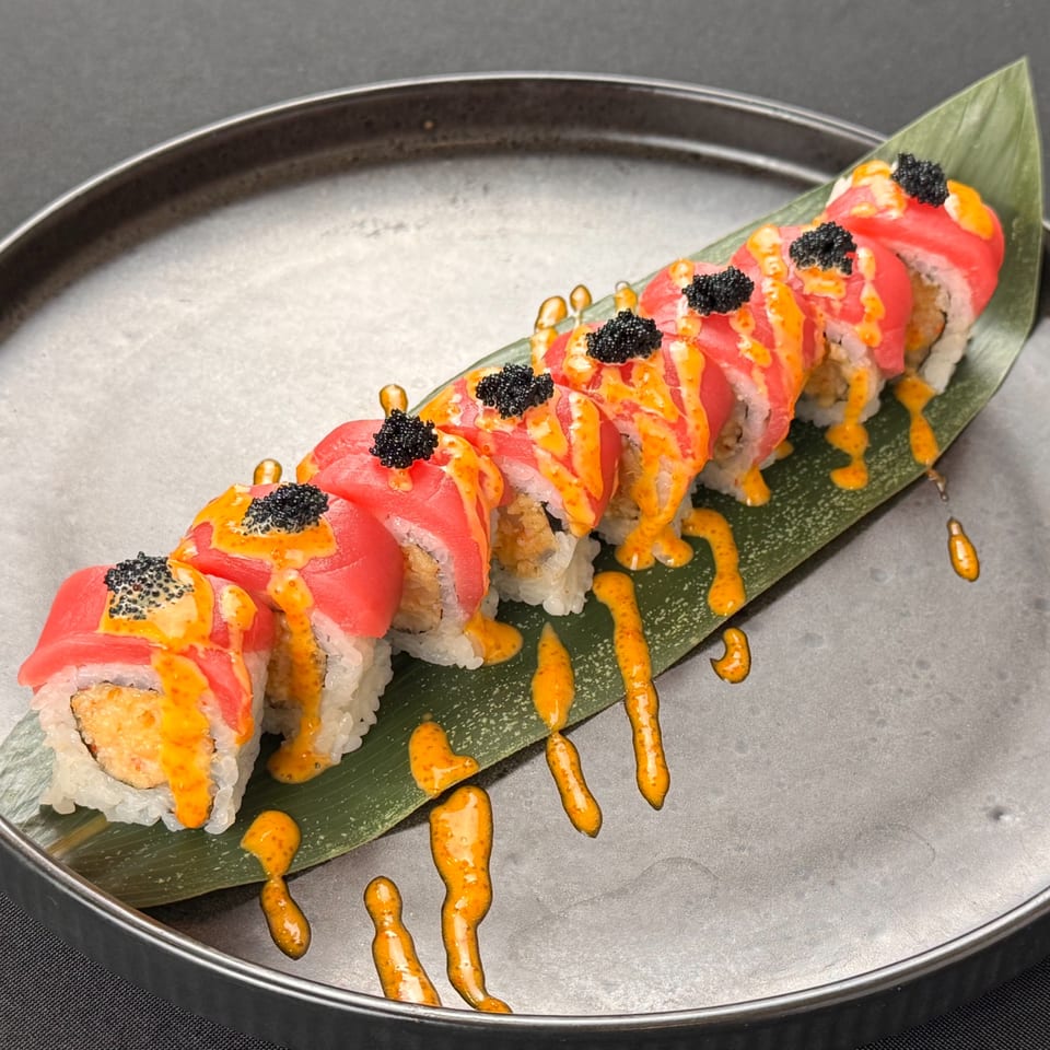 A sushi roll with tuna, orange sauce, and black caviar on a banana leaf.