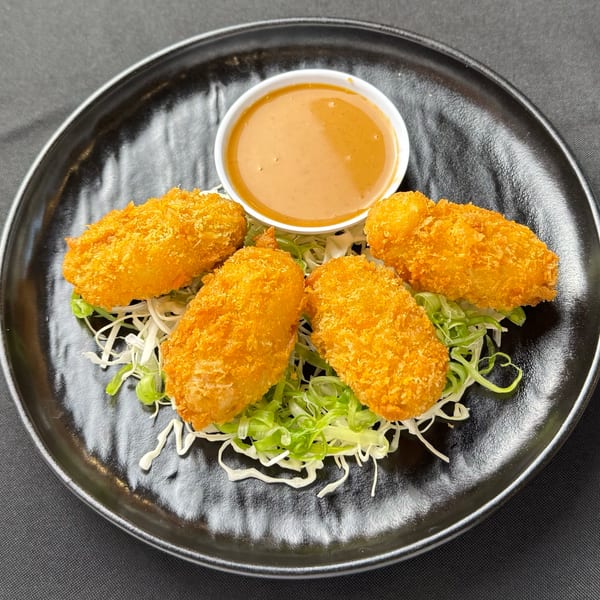 Four golden-fried shrimp tempura pieces with a side of peanut sauce on a bed of shredded cabbage.