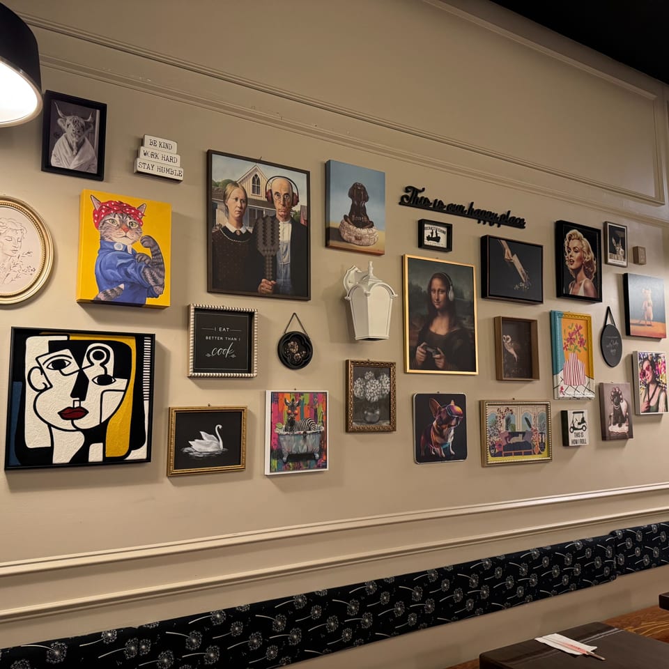 Eclectic gallery wall with various framed artworks, including humorous animal portraits and classic art parodies.