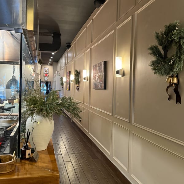 A restaurant hallway with wainscoting, modern wall sconces, and festive green wreaths with bells.