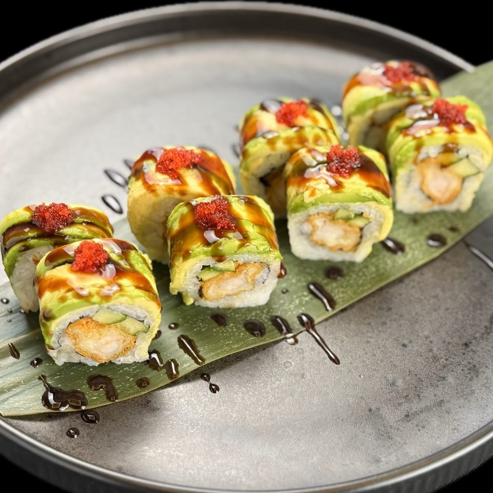 Eight pieces of sushi with avocado, tempura shrimp, and red roe on a dark plate with a leaf.